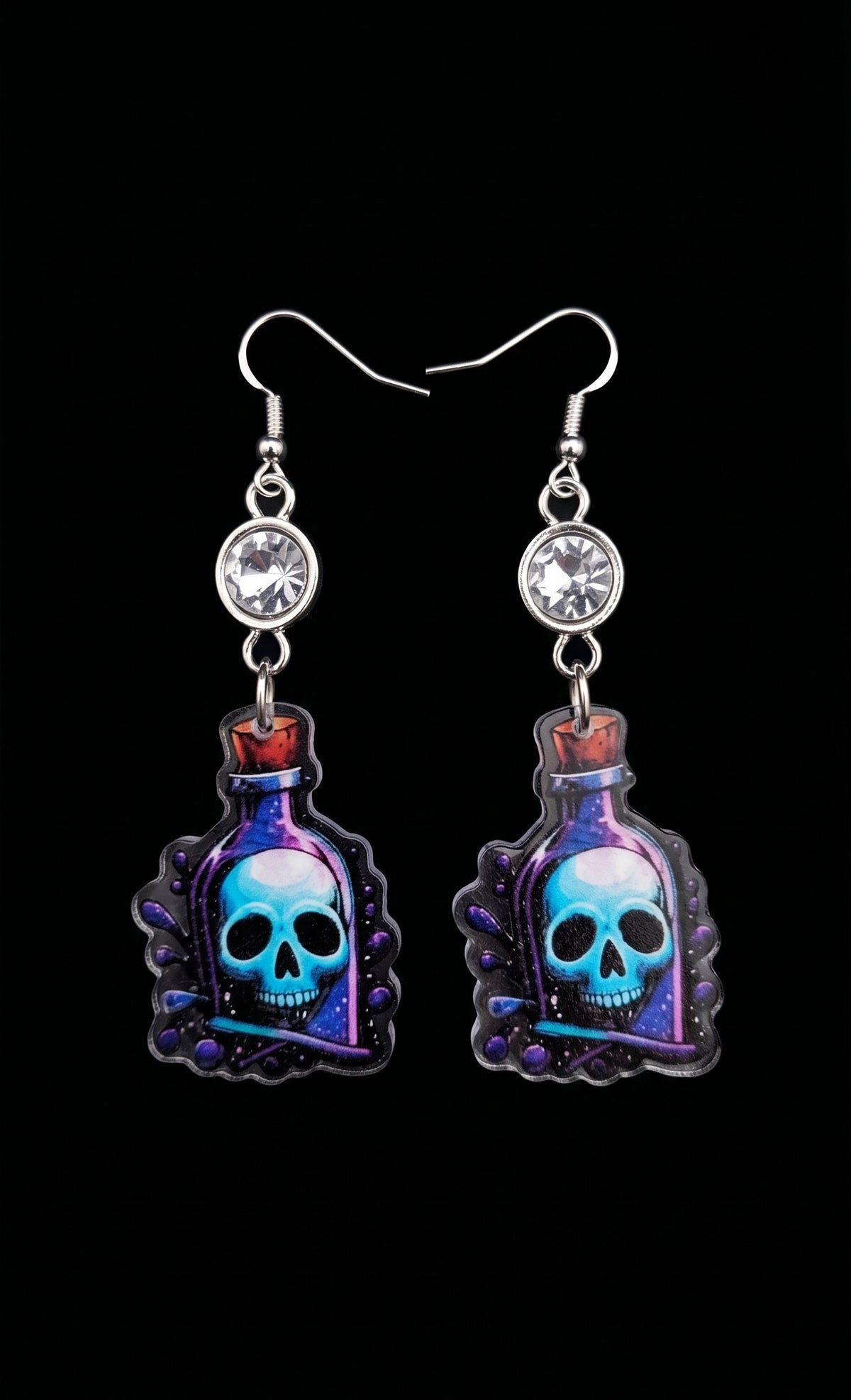 Skull Potion Earrings by Circle of Heather, full view of both earrings showing the rhinestone tops and the blue and purple potion bottle charms with skulls inside, on a plain black background.
