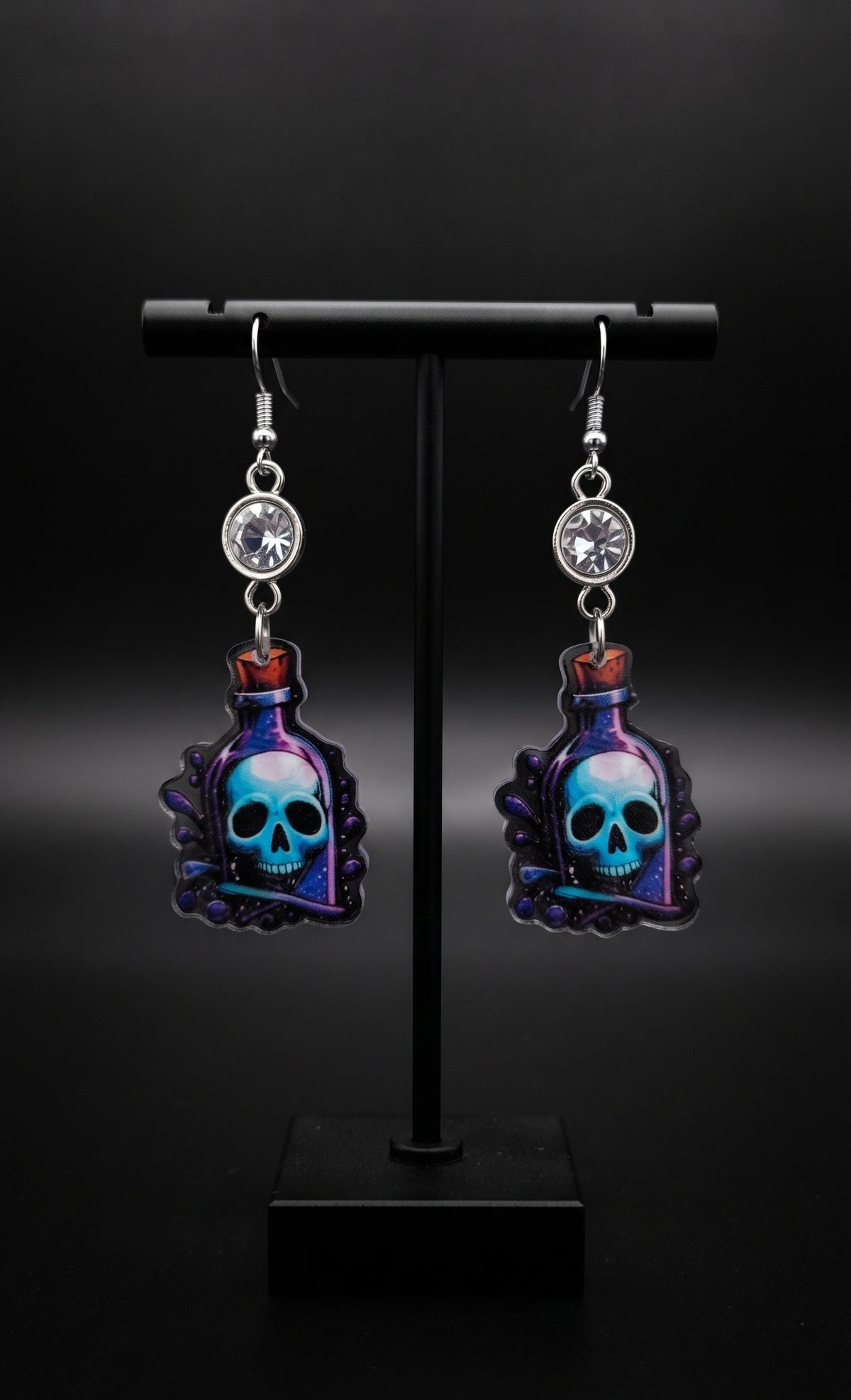 Skull Potion Earrings by Circle of Heather, angled close-up showing the painted bubbles, cork stopper and blue skull detail on the potion bottle charms, shown on the branded Circle of Heather card.