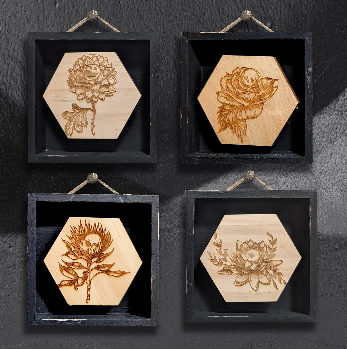 Skully Flowers miniature framed series by CamiThunderInk, laser etched wood botanical illustrations with a skull at the center of each flower, in small 4x4 frames, showing all four designs: dahlia, rose, protea, and lotus