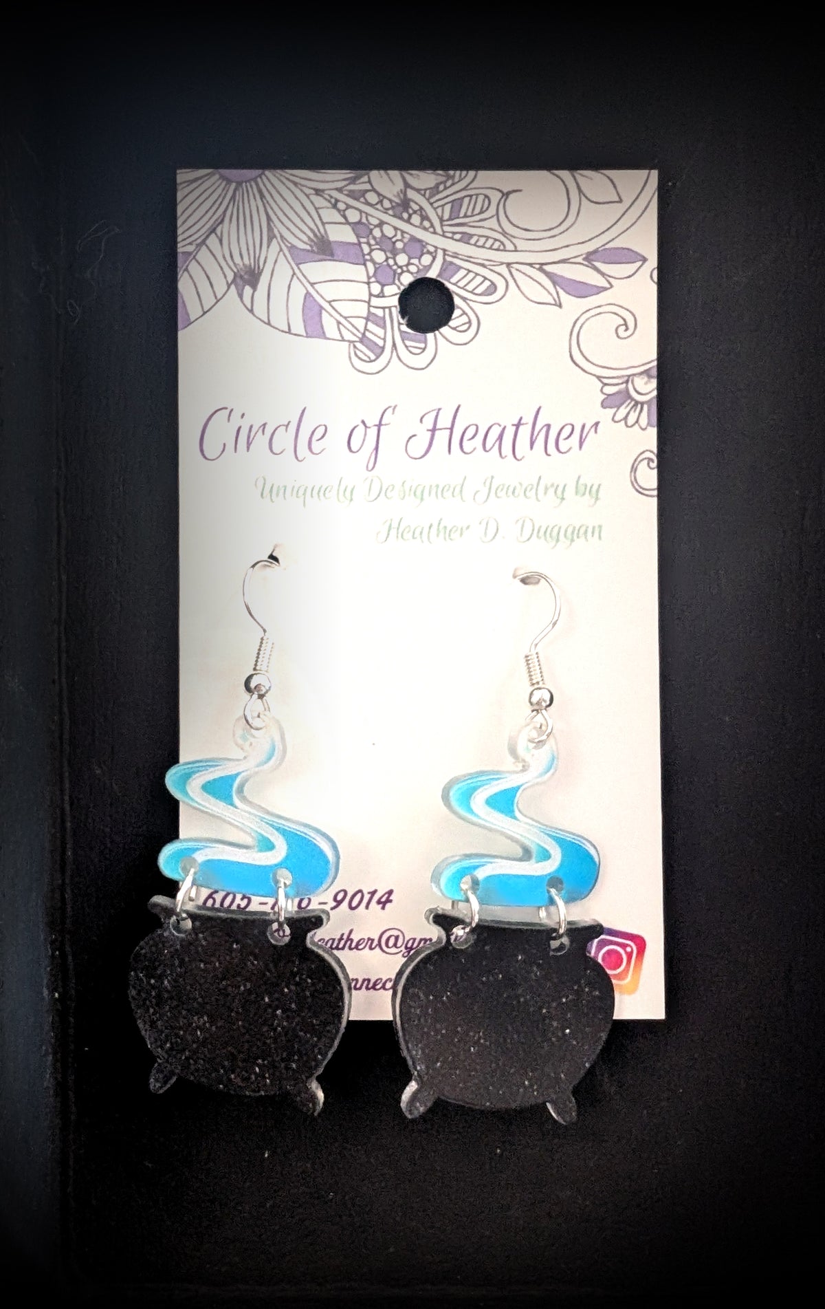 Smoking Cauldron Earrings by Circle of Heather, black glitter acrylic cauldron charms with blue and white swirled smoke toppers and silver-tone earwires, shown on the branded Circle of Heather card.