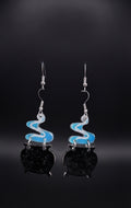 Smoking Cauldron Earrings by Circle of Heather, black glitter cauldron charms with blue and white smoke toppers and silver-tone earwires, hanging on a black T-bar jewelry stand against a dark background with blue backlight.