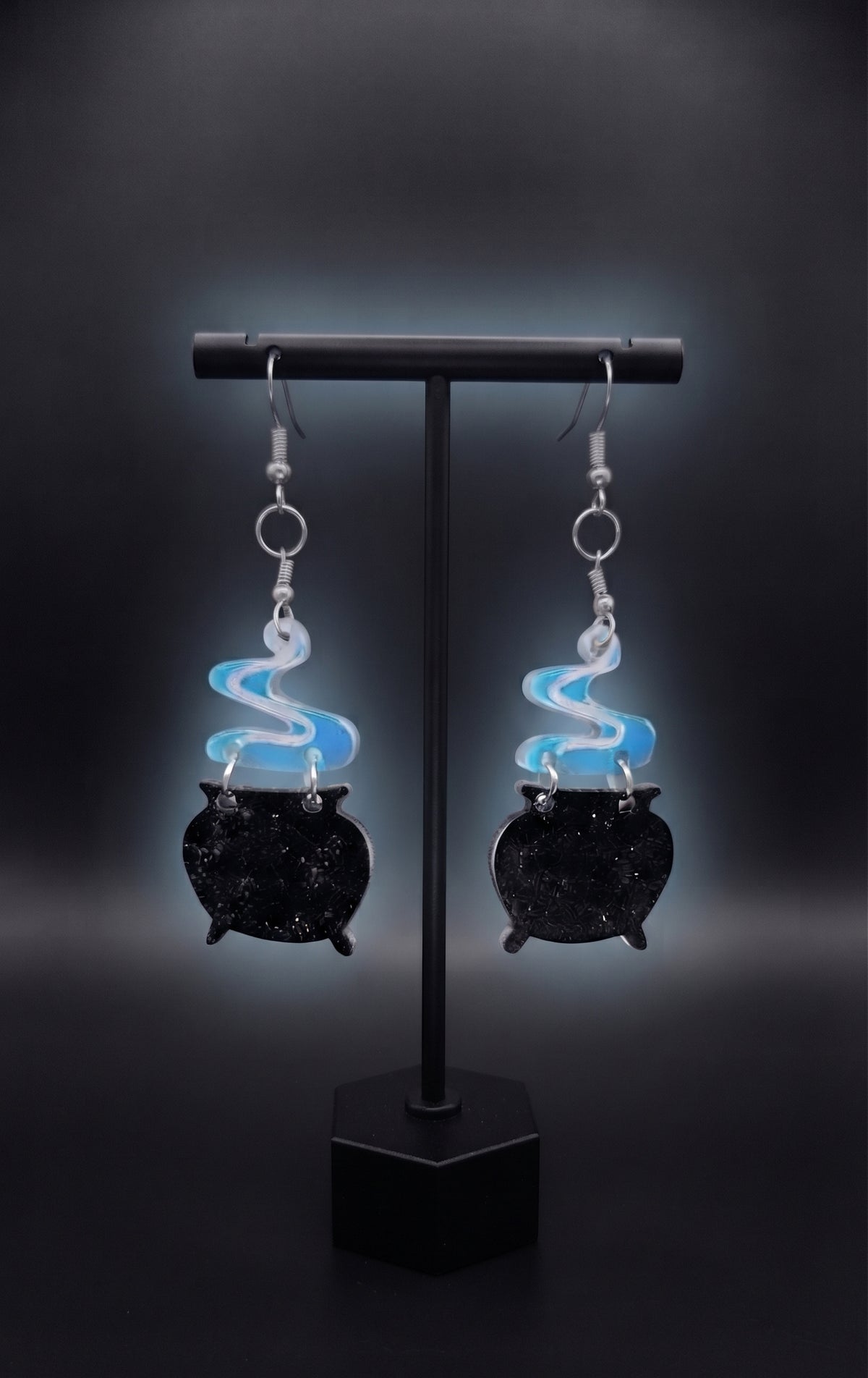 Smoking Cauldron Earrings by Circle of Heather, full view of both earrings showing the blue and white swirled smoke and black cauldron charms with silver-tone hardware, on a plain dark background.