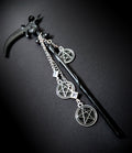An angled, close-up product shot of the black scythe hair pick against a dark background. It highlights the curve of the glossy black blade, the black cabochon setting, and the three dangling silver pentacle charms connected by rhinestone links.