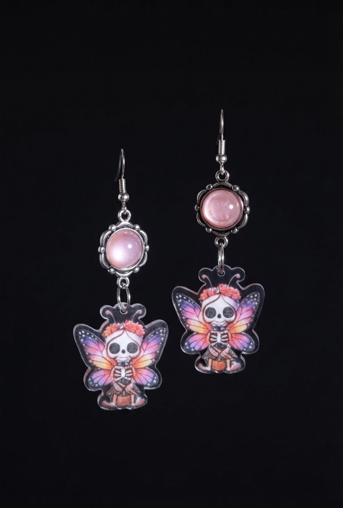 Sweet Pink Skull Fairy Earrings by Circle of Heather, full view of both earrings showing the pink cabochon tops and skull fairy charms with purple, pink and orange butterfly wings, on a plain black background.