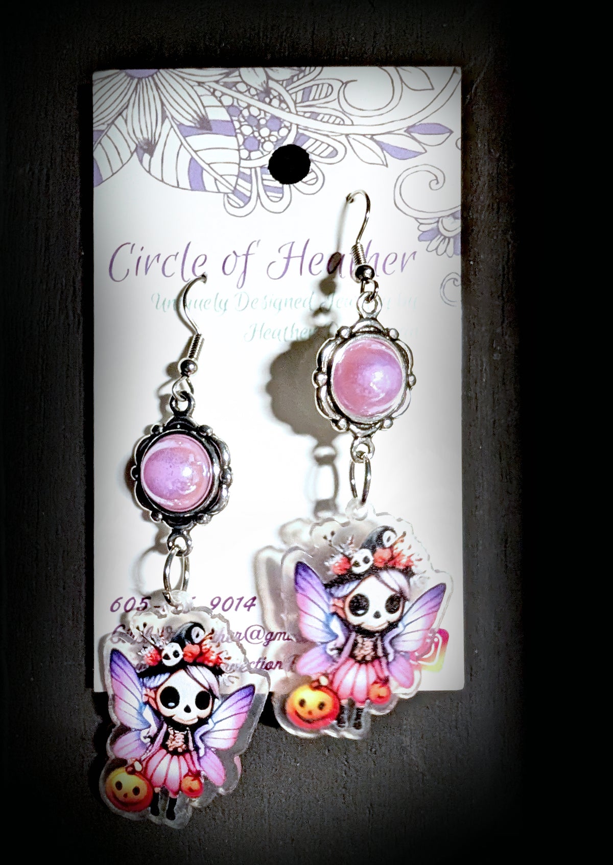 Treat Skull Fairy Earrings by Circle of Heather, pearly pink cabochons in ornate silver-tone settings above printed acrylic skull fairy charms with jack-o-lanterns, shown on the branded Circle of Heather card.
