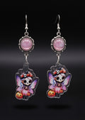 Treat Skull Fairy Earrings by Circle of Heather, full view of both earrings showing the pink cabochon tops and skull fairy charms with pink and purple wings, pink tutus and jack-o-lanterns, on a plain black background.
