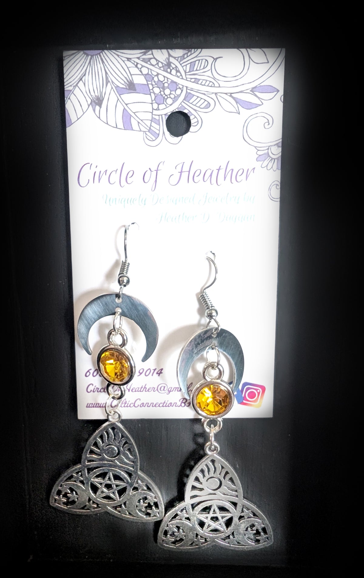 Trinity Lunar Glow Earrings by Circle of Heather, both earrings shown on the branded Circle of Heather card with crescent moons, amber stones and cut trinity knot charms.