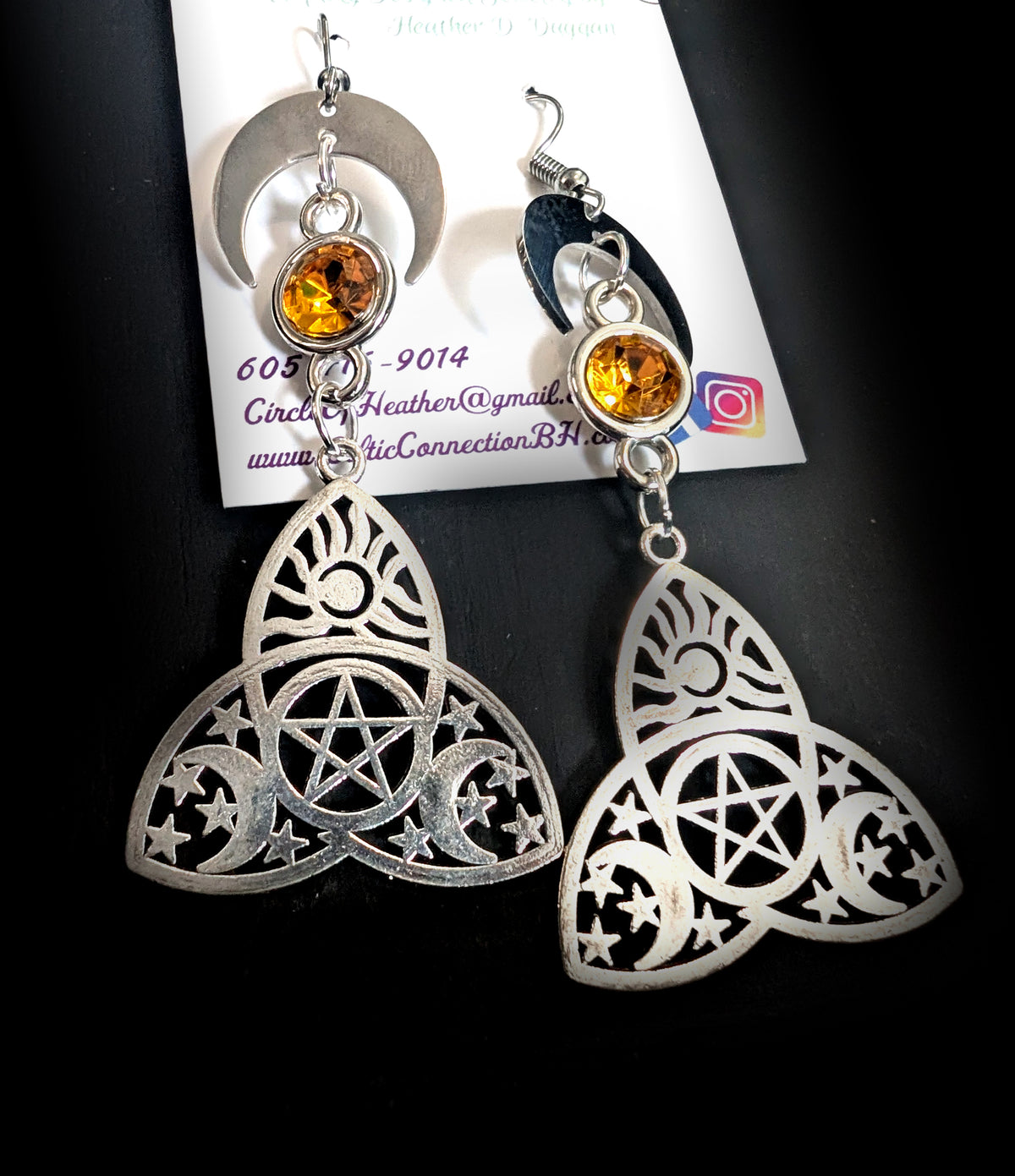 Trinity Lunar Glow Earrings by Circle of Heather, angled close-up showing the pentacle at the center of the trinity knot and the crescent moons and stars cut into each lobe, shown on the branded Circle of Heather card.