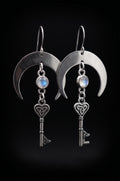 Unlock the Moon Earrings by Circle of Heather, full view of both earrings showing the brushed crescent moons, blue flash in the opalescent stones and the heart-topped skeleton keys, on a plain black background.