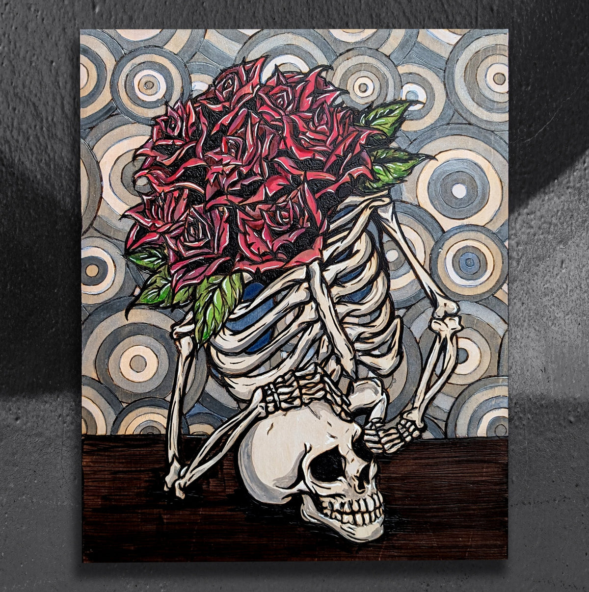 Another view of Vertigo Mortem by CamiThunderInk, an original pyrography and watercolor painting on pine showing a skeletal figure at the center of a swirling background, surrounded by bright pink roses