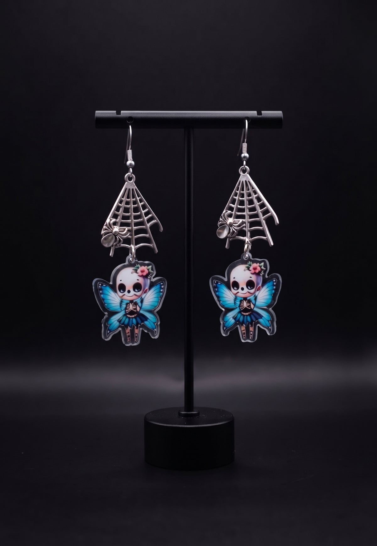 Webbed Skull Fairy Earrings by Circle of Heather, angled close-up showing the skeleton ribcage detail, striped stockings and blue butterfly wings on the printed acrylic fairy charms, shown on the branded Circle of Heather card.