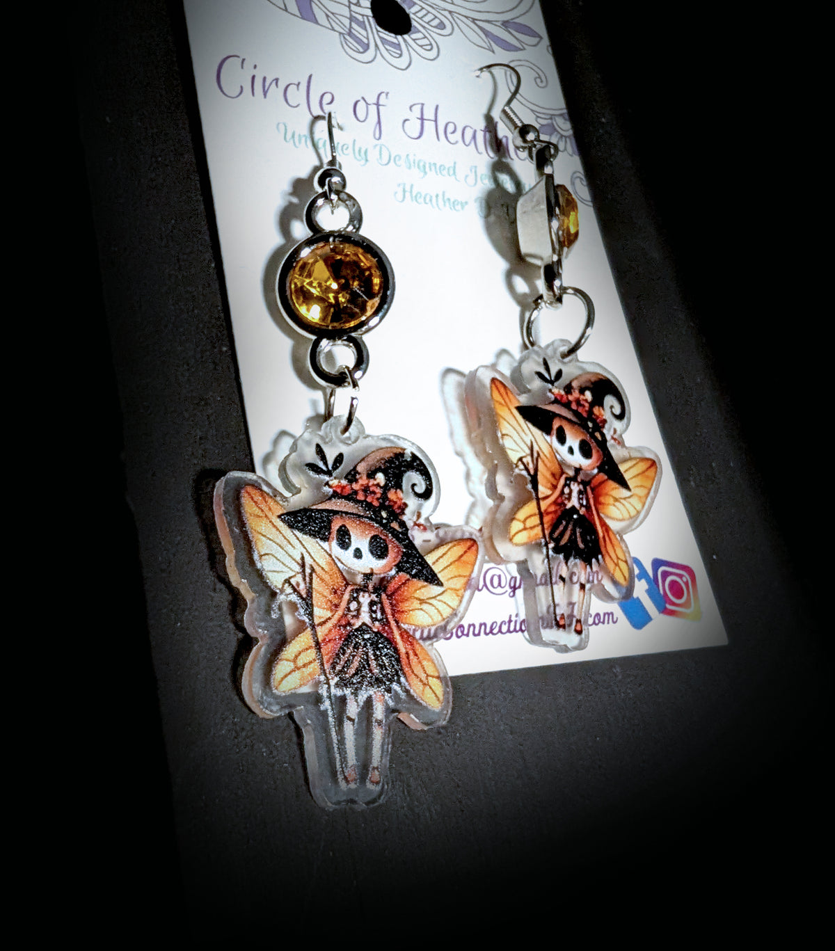 Witchy Skull Fairy Earrings by Circle of Heather, angled close-up showing the wing veining, corset bodice and flower-trimmed witch hat on the printed acrylic charms, shown on the branded Circle of Heather card.