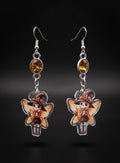 Witchy Skull Fairy Earrings by Circle of Heather, full view of both earrings showing the amber stone tops and skull fairy charms with flower-trimmed witch hats, orange wings and brooms, on a plain black background.