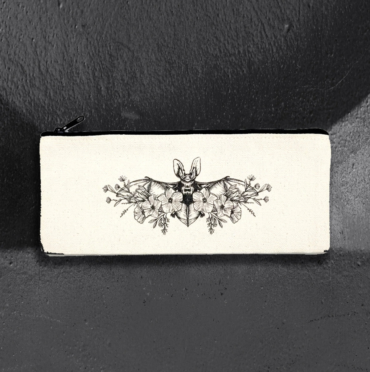 Floral Bat canvas pencil case by CamiThunderInk, a cream canvas zip pouch printed in black ink with a long eared bat over open blooms, with a black zipper