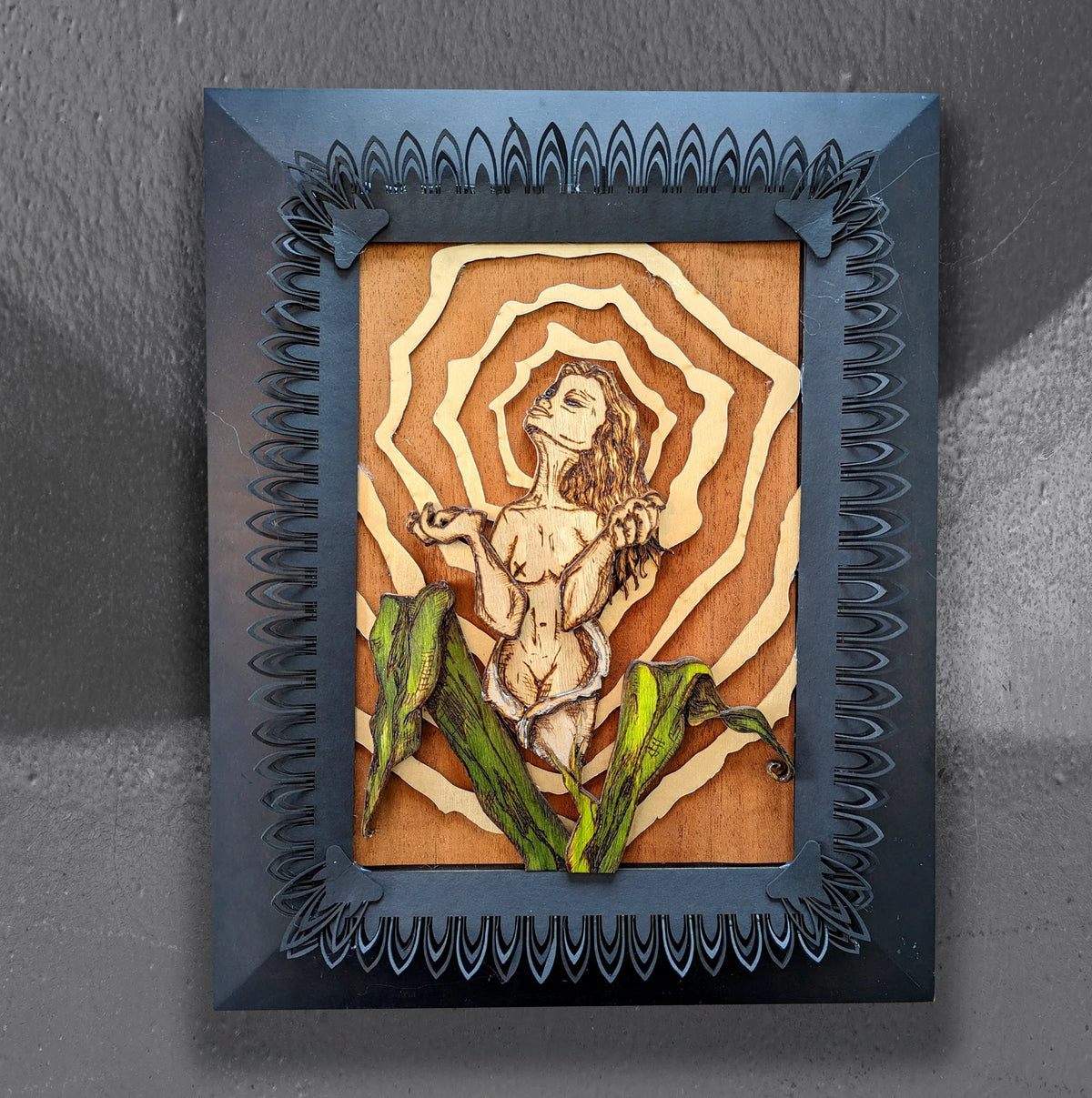 Birth of a Calla Lily by CamiThunderInk, an original layered relief artwork of a woman burned and watercolored on laser cut birch, surrounded by gold rays and mounted on a recycled cabinet door with a black border