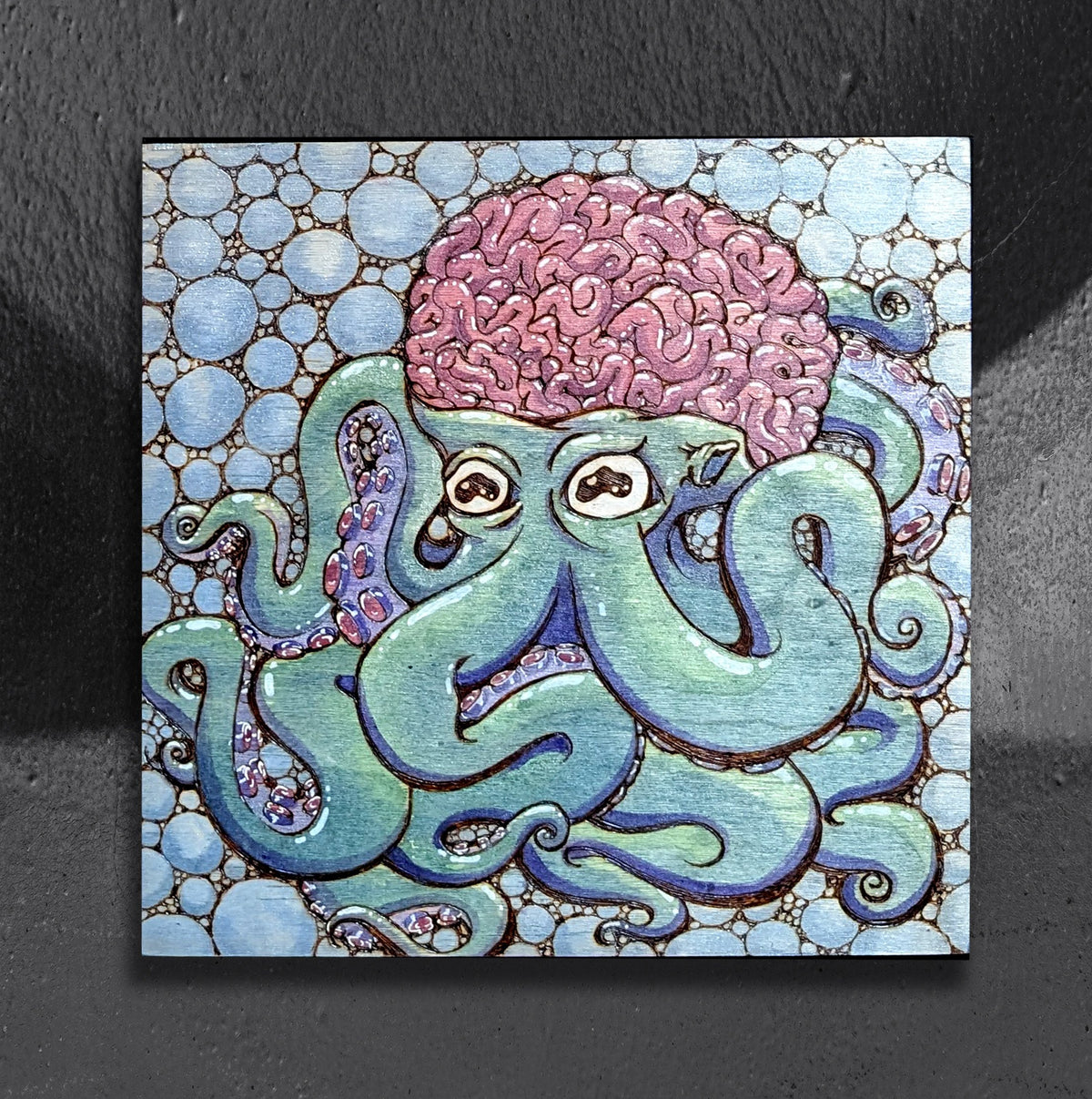 Bubbles and Brains by CamiThunderInk, an original pyrography, watercolor, and ink painting on wood of a blue and purple octopus with a brain for a head, surrounded by bubbles