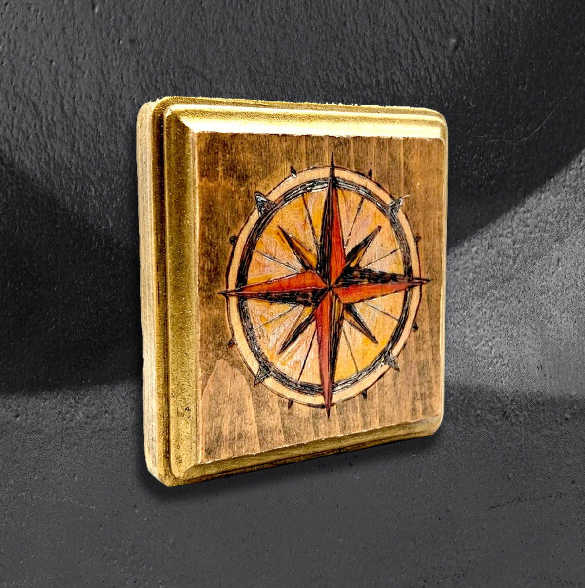 Compass flash block by CamiThunderInk, a small reclaimed pine block with a burned and painted compass rose in amber and red, with gold edging