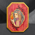 Hestia's Hearth by CamiThunderInk, an original pyrography and acrylic painting on a wood canvas showing the goddess Hestia holding a steady flame, framed by wood burned filigree and a metallic gold beveled edge