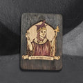 The Hierophant by CamiThunderInk, an original pyrography and watercolor tarot card on a thin wood panel, showing a crowned figure in purple robes raising one hand and holding a triple cross staff, framed by an arched halo with a banner reading The Hierophant, photographed on a gray textured background