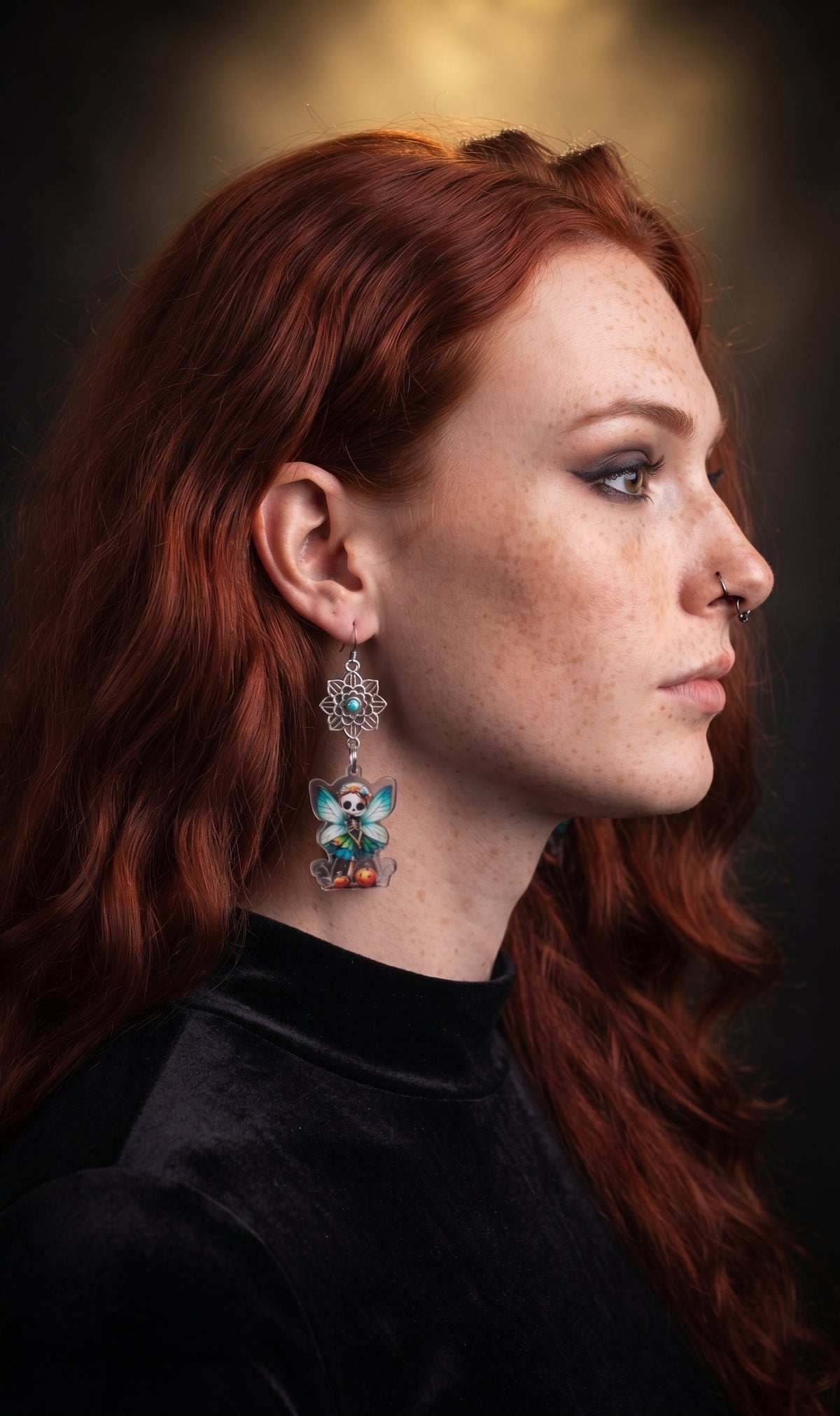 Mandala Pumpkin Skull Fairy Earrings by Circle of Heather worn by a model with long red hair and a black mock neck top, silver mandala flower with turquoise center above a printed skull fairy charm with teal wings and pumpkins.
