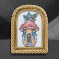 Mushie House framed print by CamiThunderInk, a whimsical mushroom cottage illustration topped with a winged insect, in a small arched gold frame with rope and bead trim