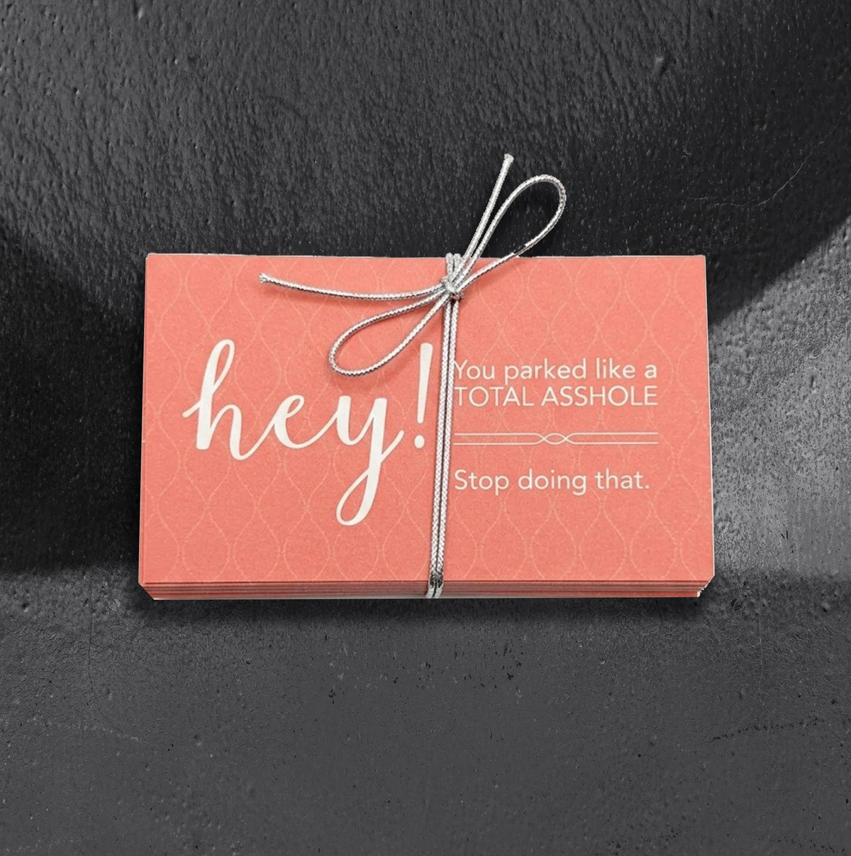 Pink passive aggressive parking cards by Reclamation Tattoo and Oddities, a 25 pack of business cards reading Hey! You parked like a total asshole. Stop doing that., tied with a silver bow