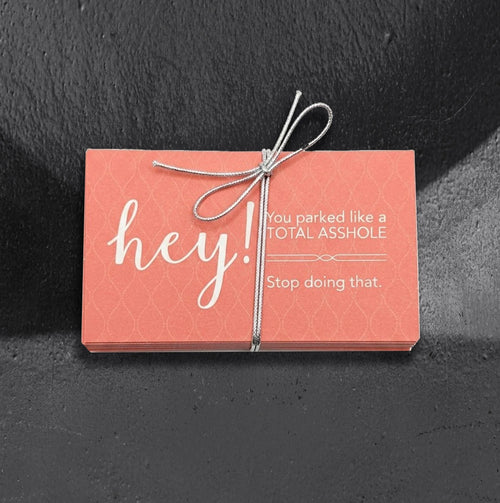 Pink passive aggressive parking cards by Reclamation Tattoo and Oddities, a 25 pack of business cards reading Hey! You parked like a total asshole. Stop doing that., tied with a silver bow