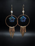 A pair of bohemian-style gold-tone hoop earrings with a central iridescent blue and purple pentagram star, a small round white stone, and a dangling fringe of thin gold-tone bars, set against a dark background.