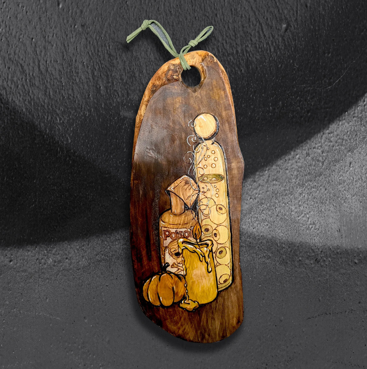 Punkins and Poisons by CamiThunderInk, an original pyrography and stain piece on a live edge olive wood board showing a dripping candle, a poison bottle, a potion, and a small pumpkin, hanging from a sage green cord