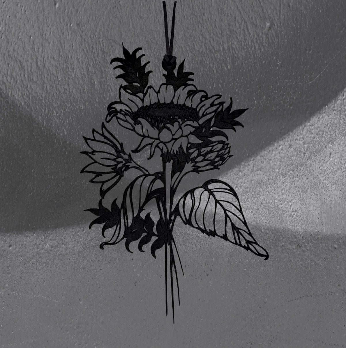 Sunflower wall hanger by CamiThunderInk, a matte black 3D printed sunflower with layered petals, smaller blooms, and long veined leaves on a thin stem