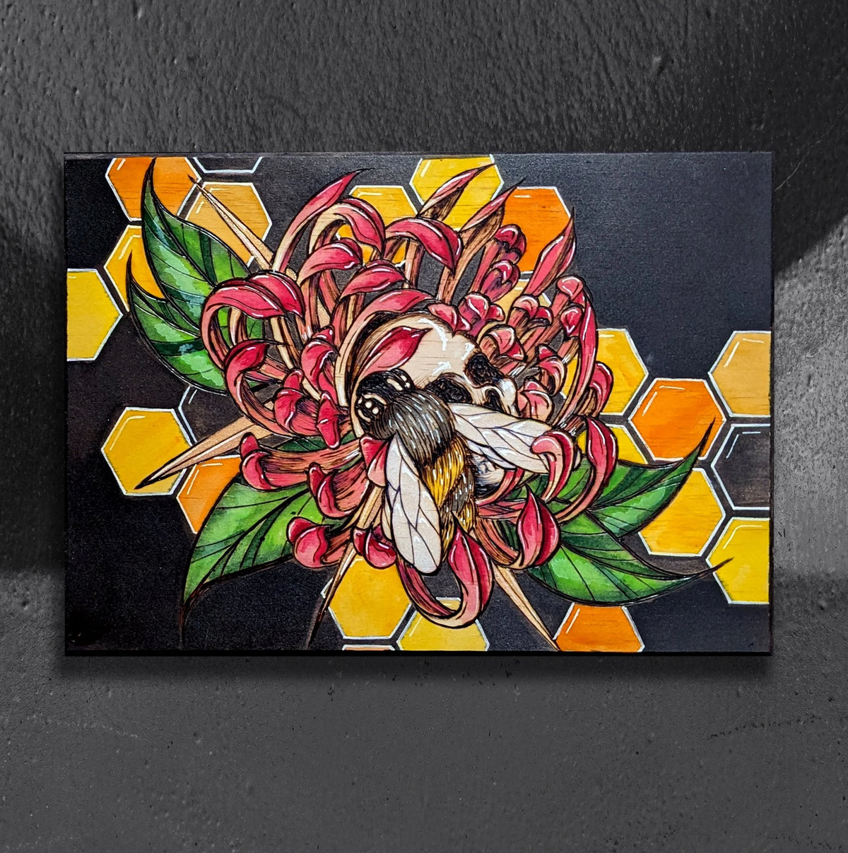 Sweet Nectar Repose by CamiThunderInk, an original pyrography, watercolor, and acrylic painting on a thick wood panel showing a large bee resting on a skull beside a yellow and pink chrysanthemum, over a honeycomb pattern