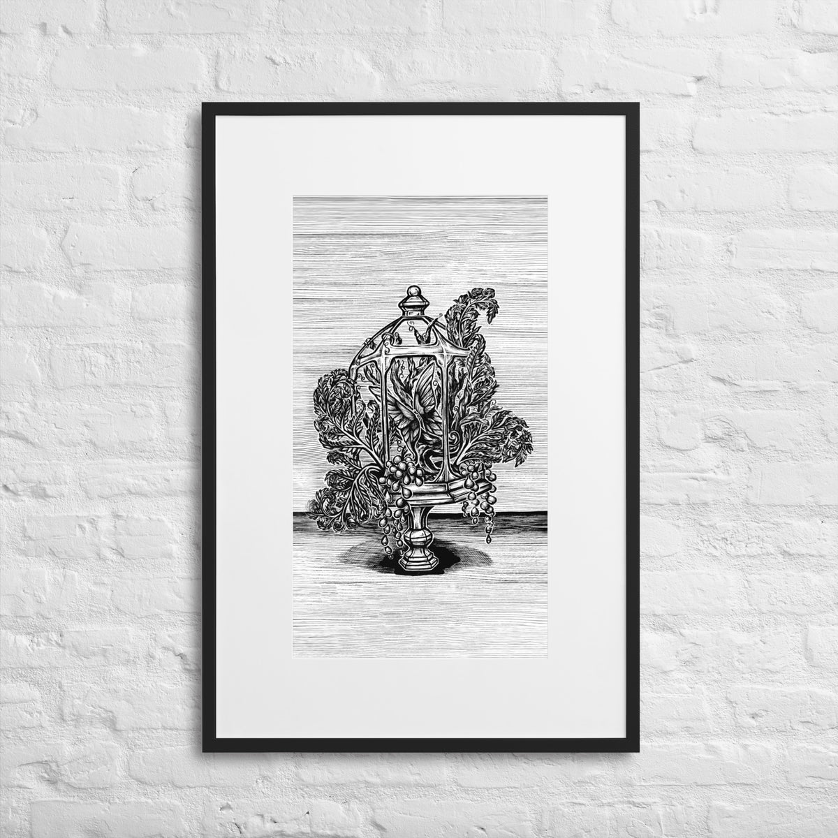 Verdant Vivarium matted framed print by CamiThunderInk, a black and white pen and ink illustration of an open terrarium on a carved pedestal, filled with ferns and string of pearls, shown with a white mat in a black frame hanging on a white painted brick wall.